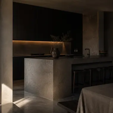 Dark kitchen with a honed stone island and a warm light cove