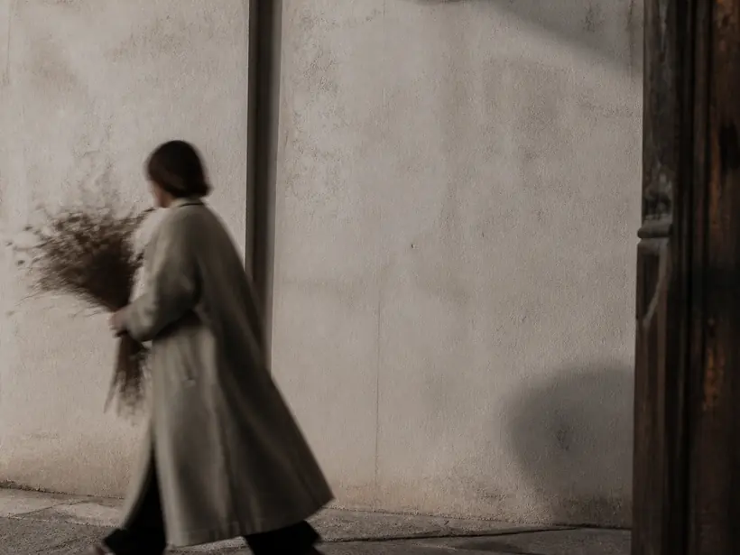 Black and white photograph of a person walking past a pale concrete wall