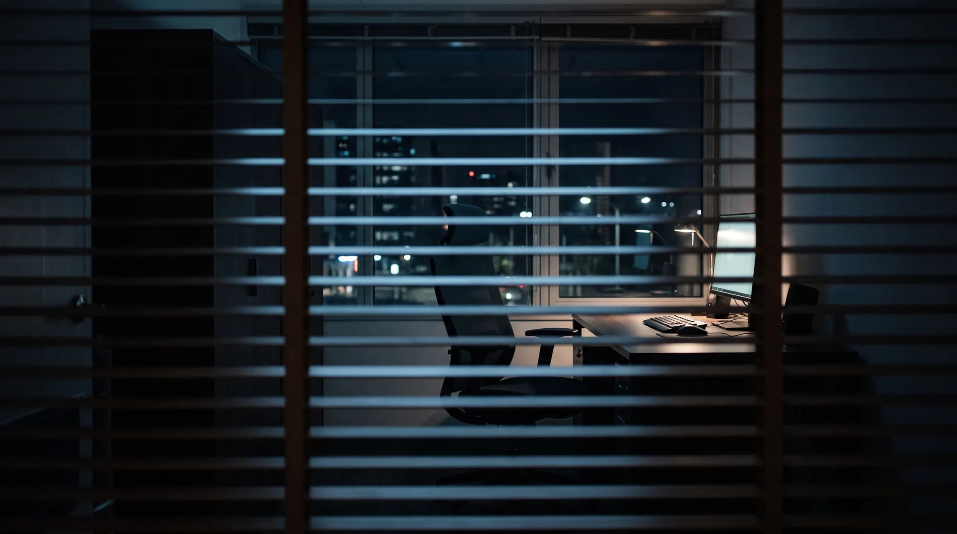 A dark office at night seen through half-closed window blinds