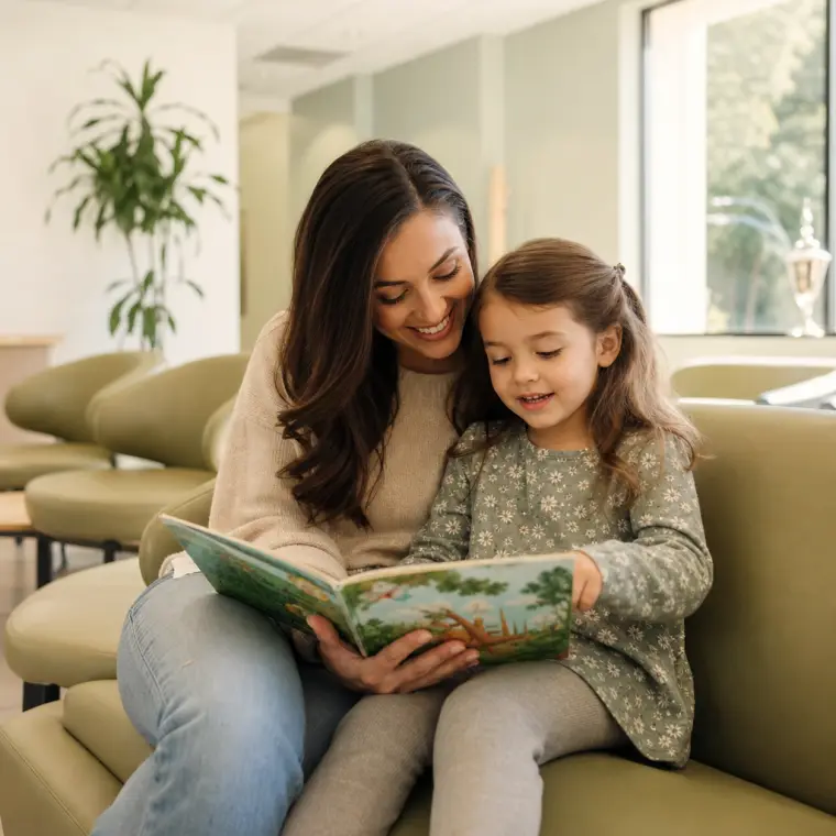 A parent and child reading together in a dental waiting room