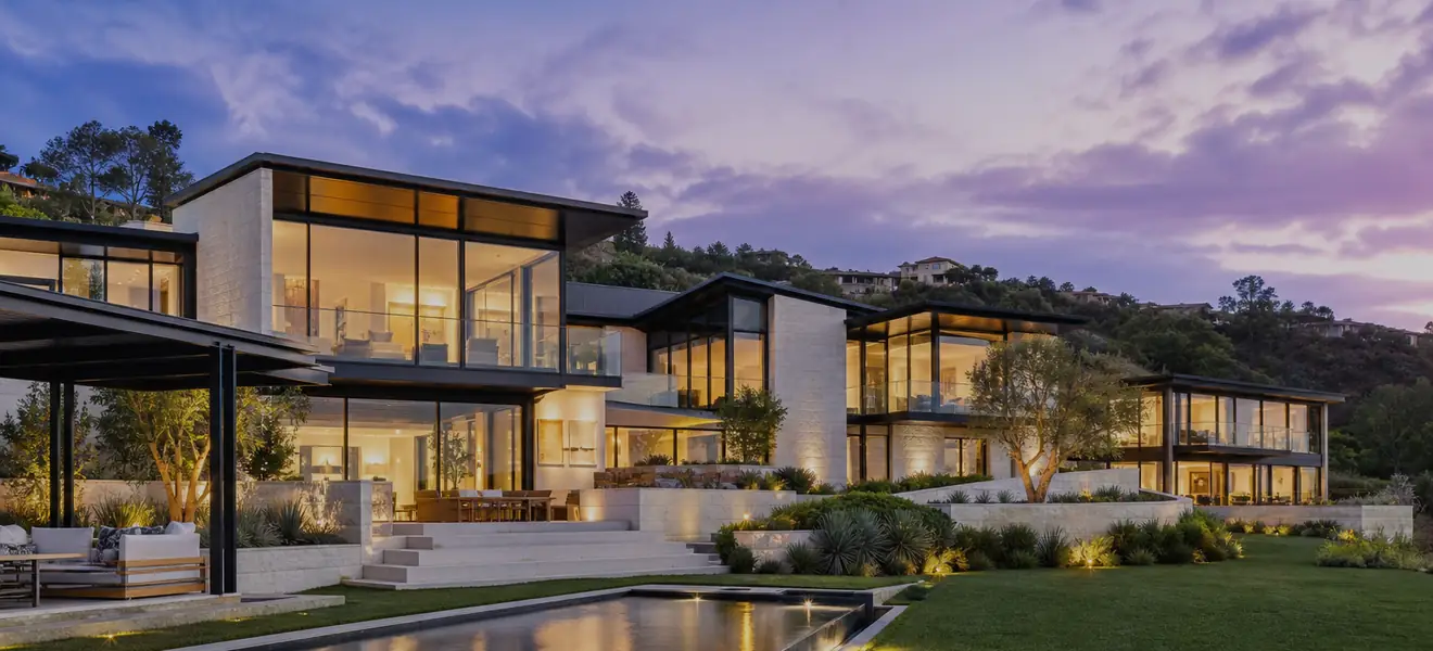 Contemporary hillside house at blue hour with lit glass walls and a reflecting pool