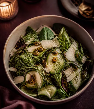 A bowl of dressed leaves with shaved cheese and cucumber