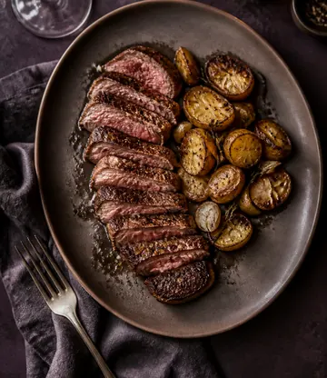 Sliced grilled beef with roast potatoes on a dark plate