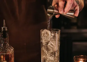 Clear spirit poured over ice into a tall glass at the bar