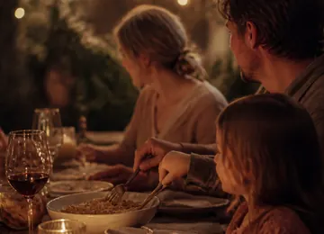 A shared bowl passed across a table under string lights