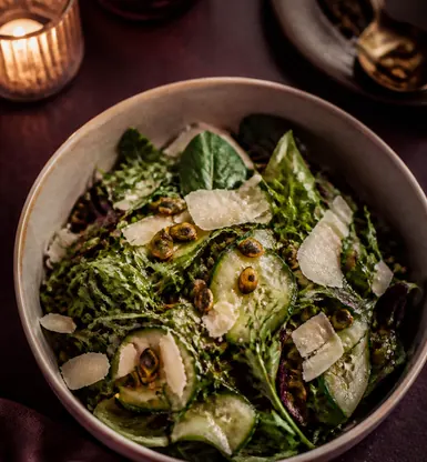 A bowl of dressed leaves with shaved cheese and cucumber