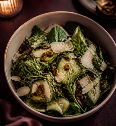 A bowl of dressed leaves with shaved cheese and cucumber