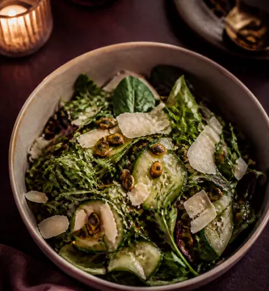 A bowl of dressed leaves with shaved cheese and cucumber