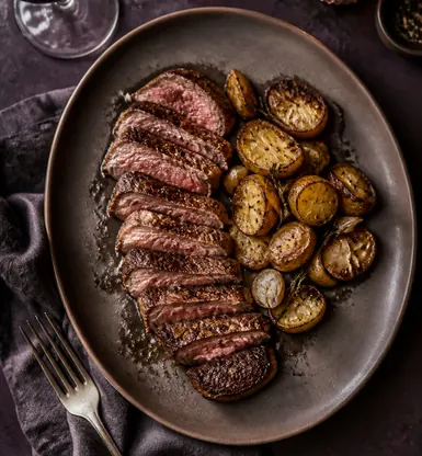 Sliced grilled beef with roast potatoes on a dark plate