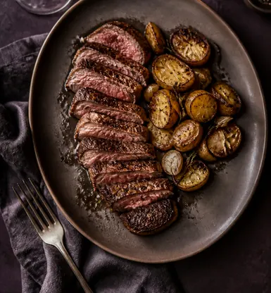 Sliced grilled beef with roast potatoes on a dark plate