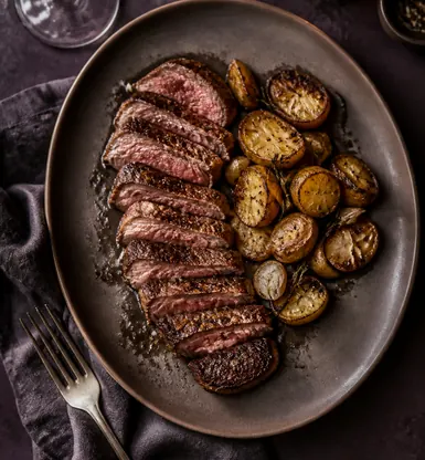 Sliced grilled beef with roast potatoes on a dark plate